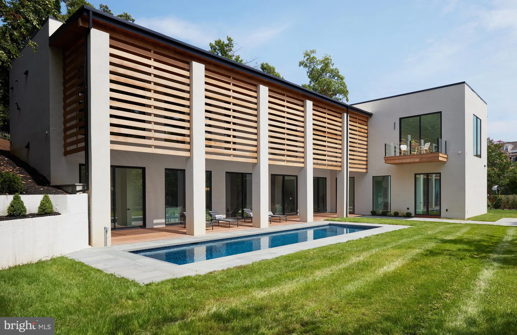 Daytime rear elevation with the lap pool, stucco walls, and wood-slat screening