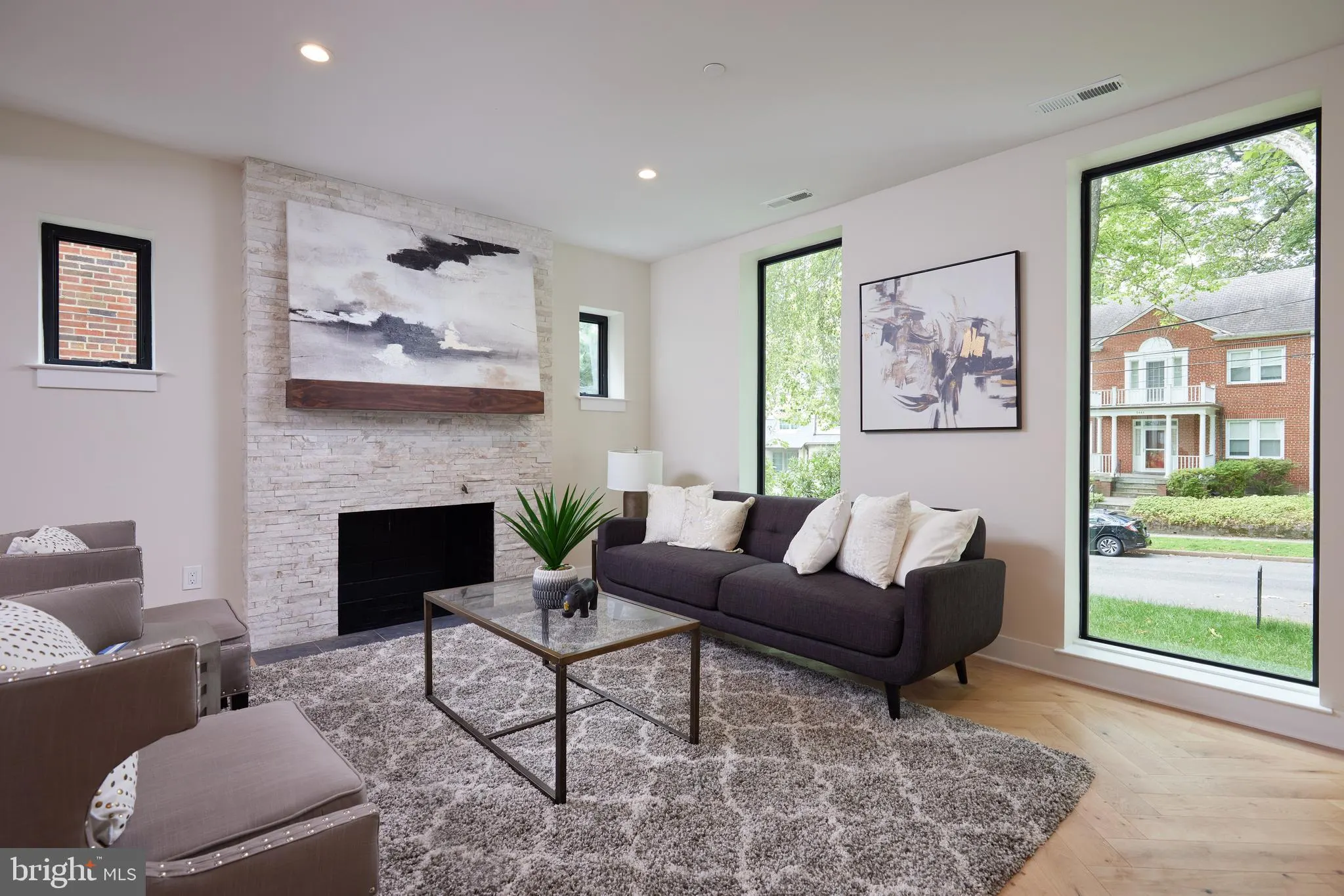 Living room with fireplace, dark sofa, and large windows to exterior