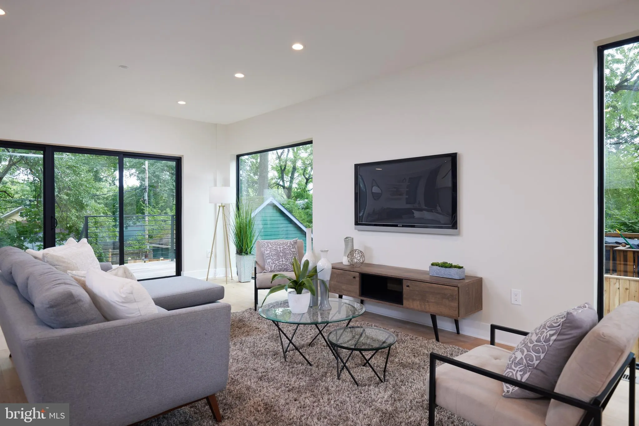 Living room with gray sectional, TV, and floor-to-ceiling windows