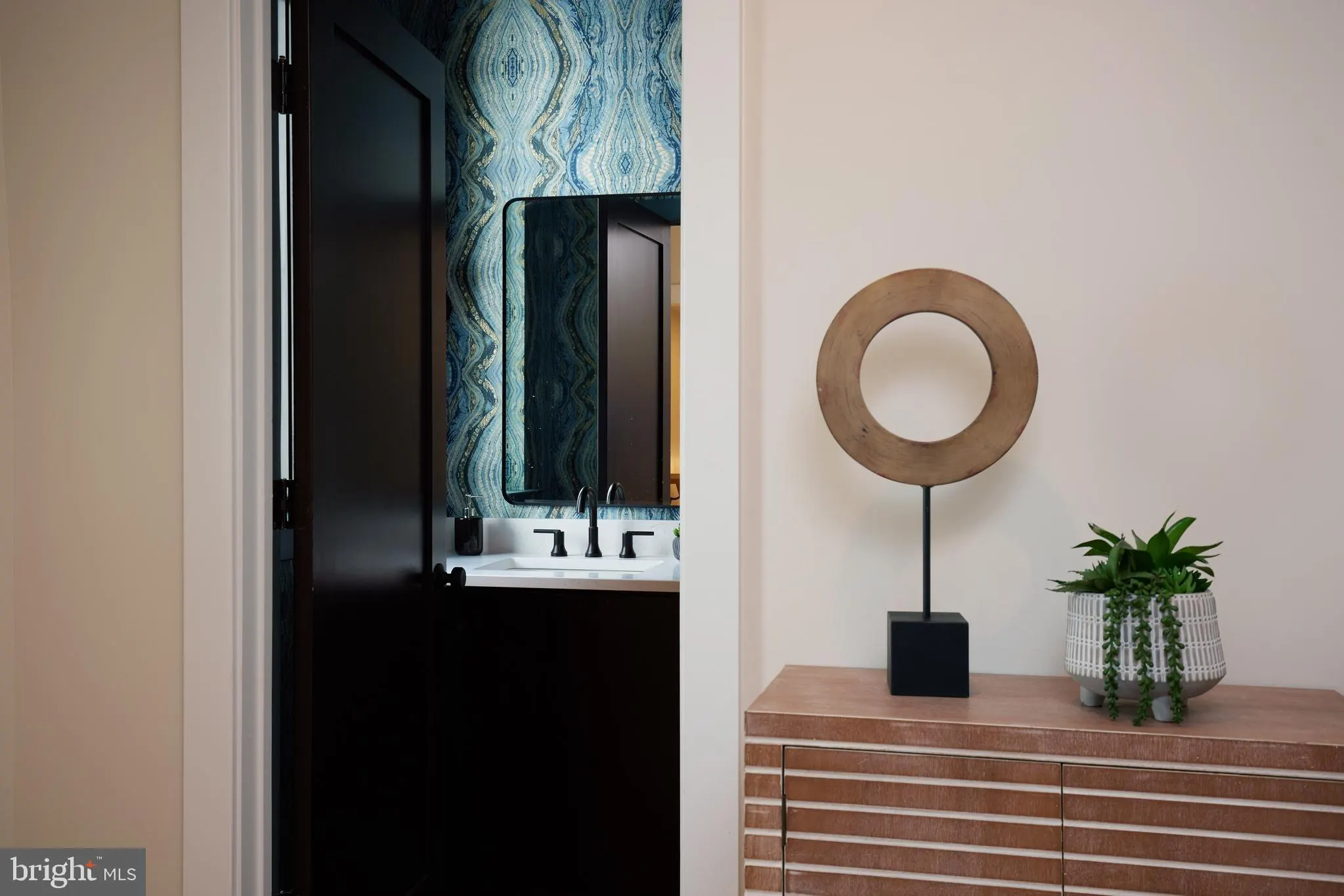 Bathroom with blue patterned wallpaper and wooden vanity with round mirror