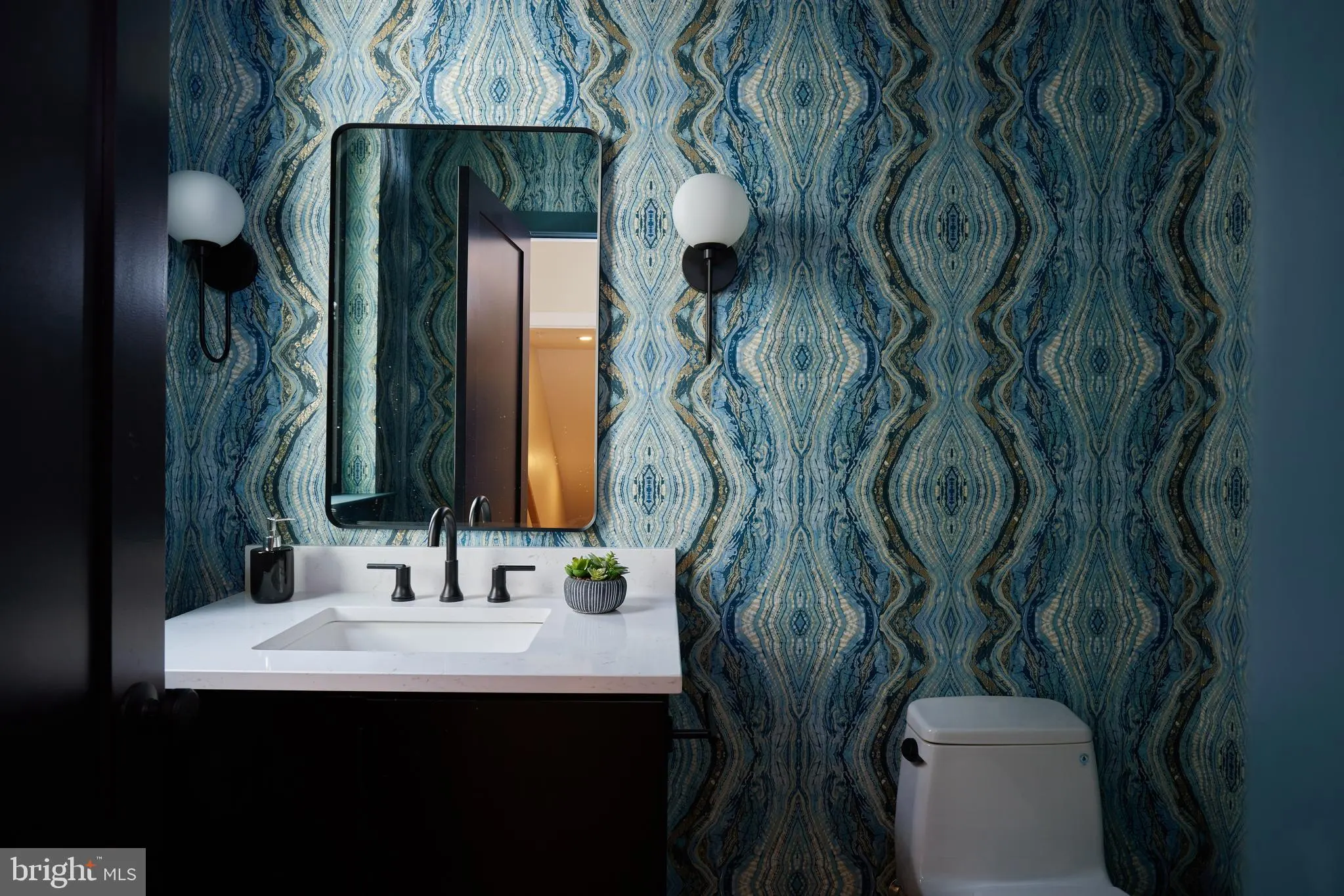 Bathroom sink with black framed mirror, white quartz countertop, patterned wallpaper