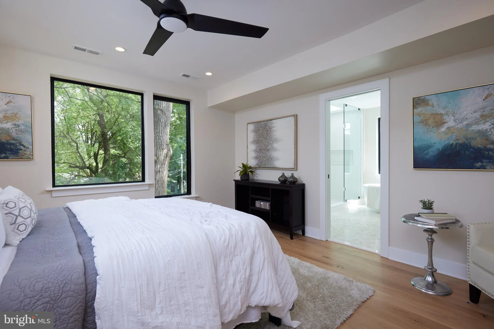 Bedroom with queen bed, black dresser, glass door to ensuite, large windows