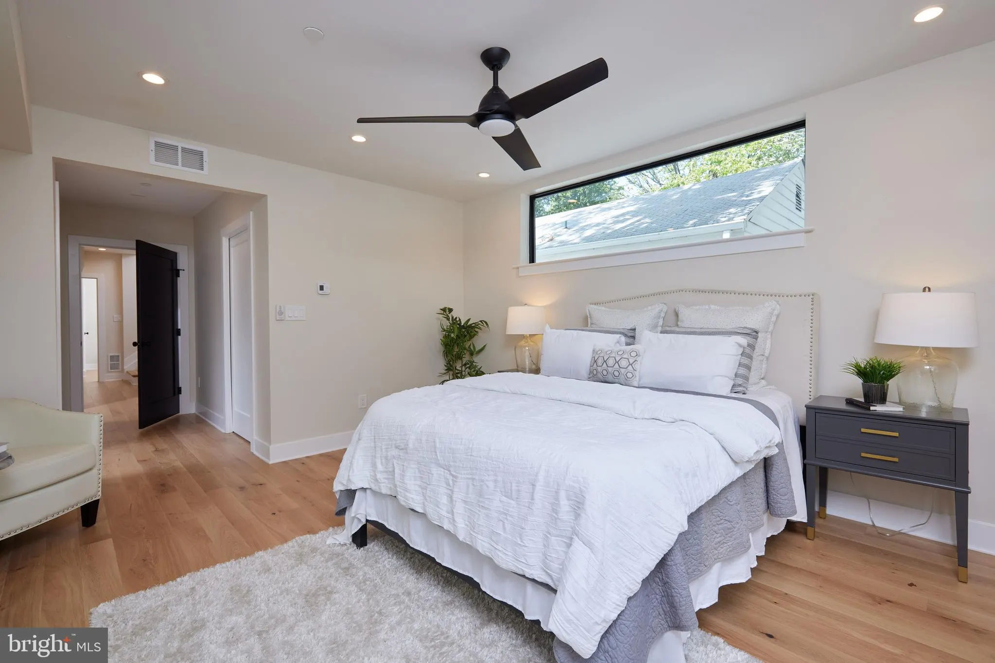 Bedroom with white linens, dark wood nightstand, clerestory window, wood flooring