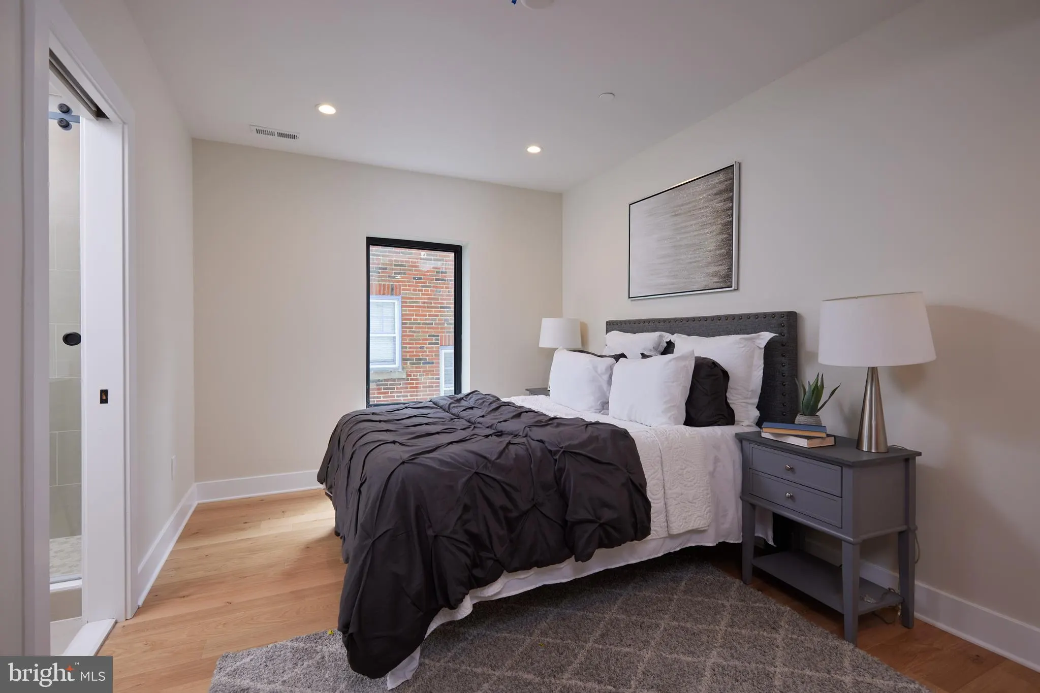 Bedroom with black and white bedding, wood flooring, nightstand