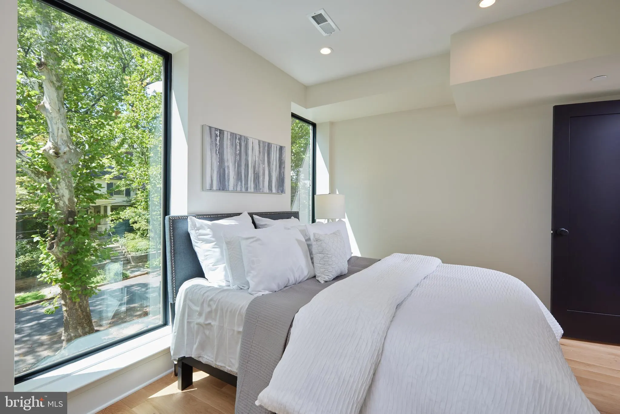Bedroom with white bedding, large windows, and wood flooring