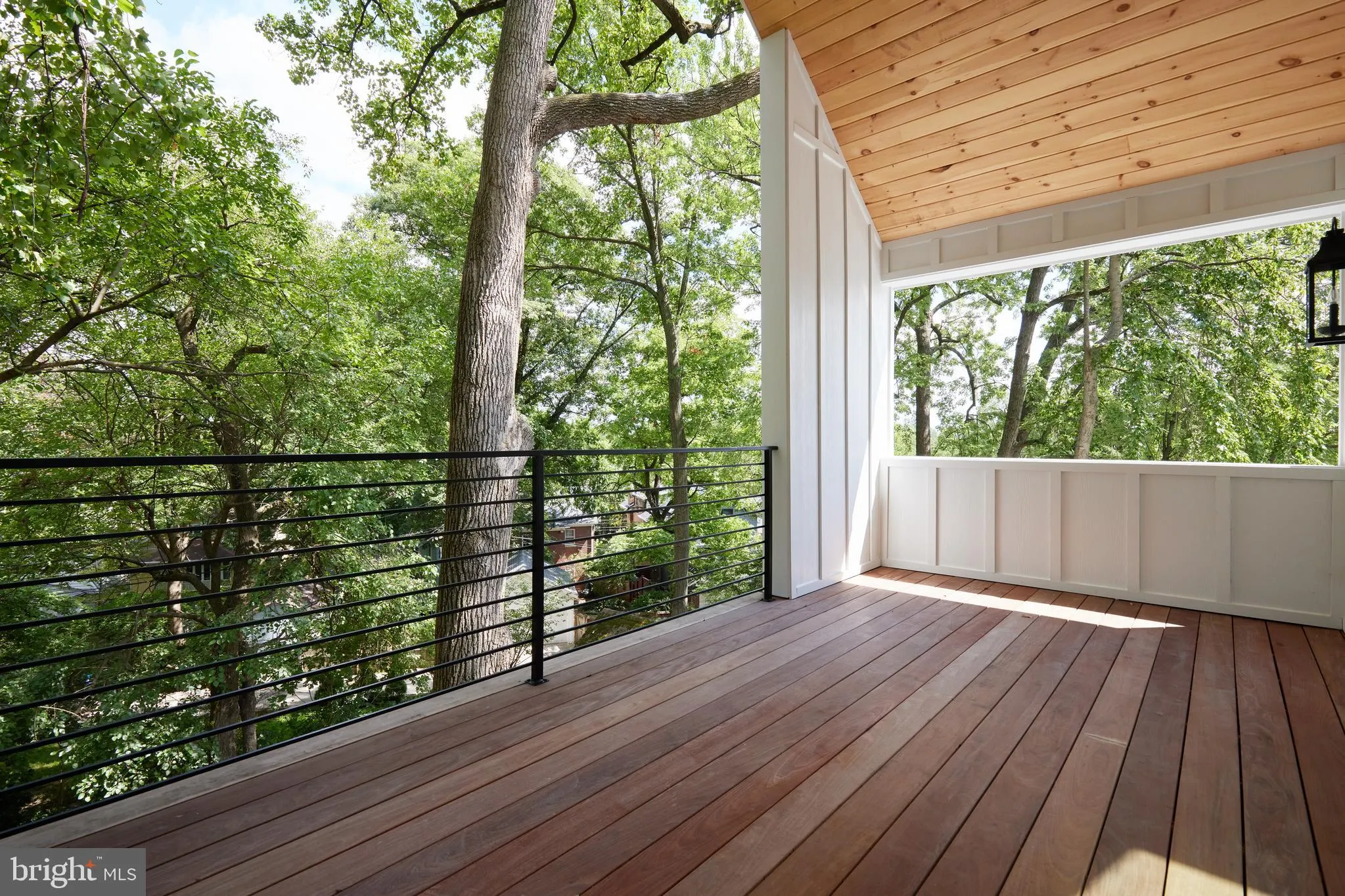 Covered deck with wood ceiling, railing, and tree canopy views