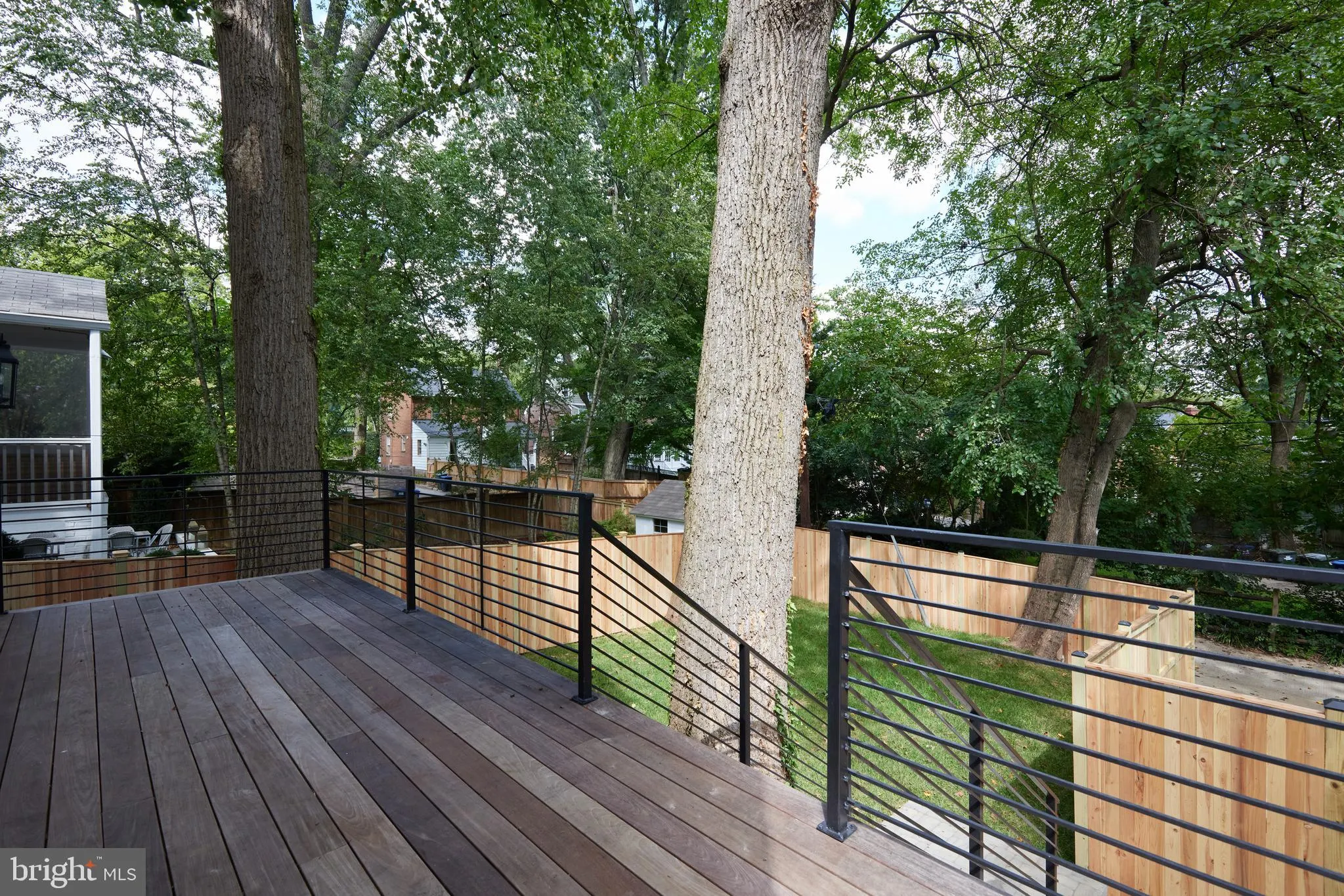 Raised composite deck with metal cable railing and mature trees