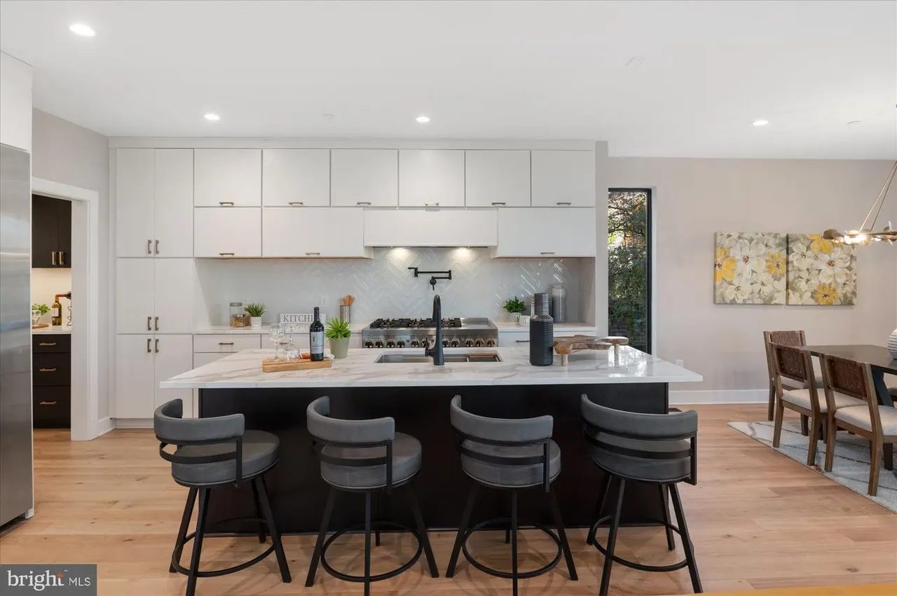 Kitchen with white cabinetry, black island, and four bar stools
