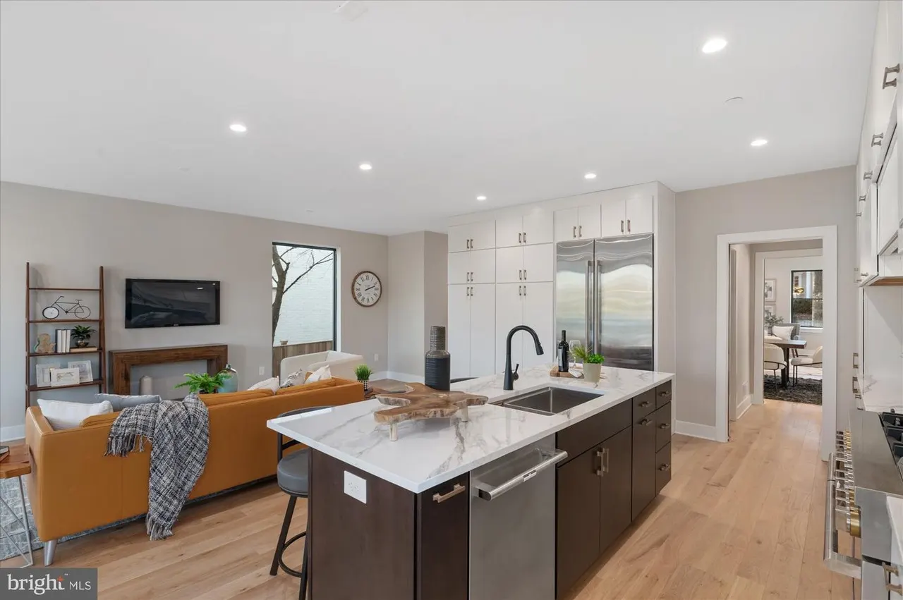 Open kitchen and living area with dark island, white upper cabinets, orange sofa