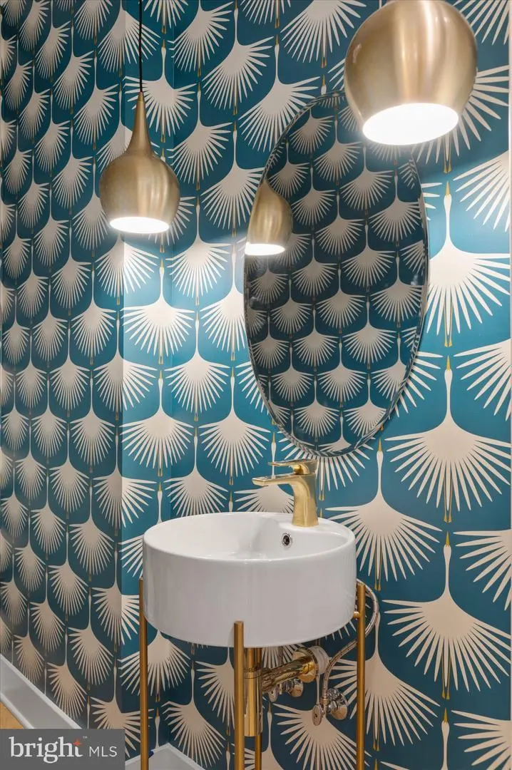 Powder room with teal patterned wallpaper and brass pendant lights