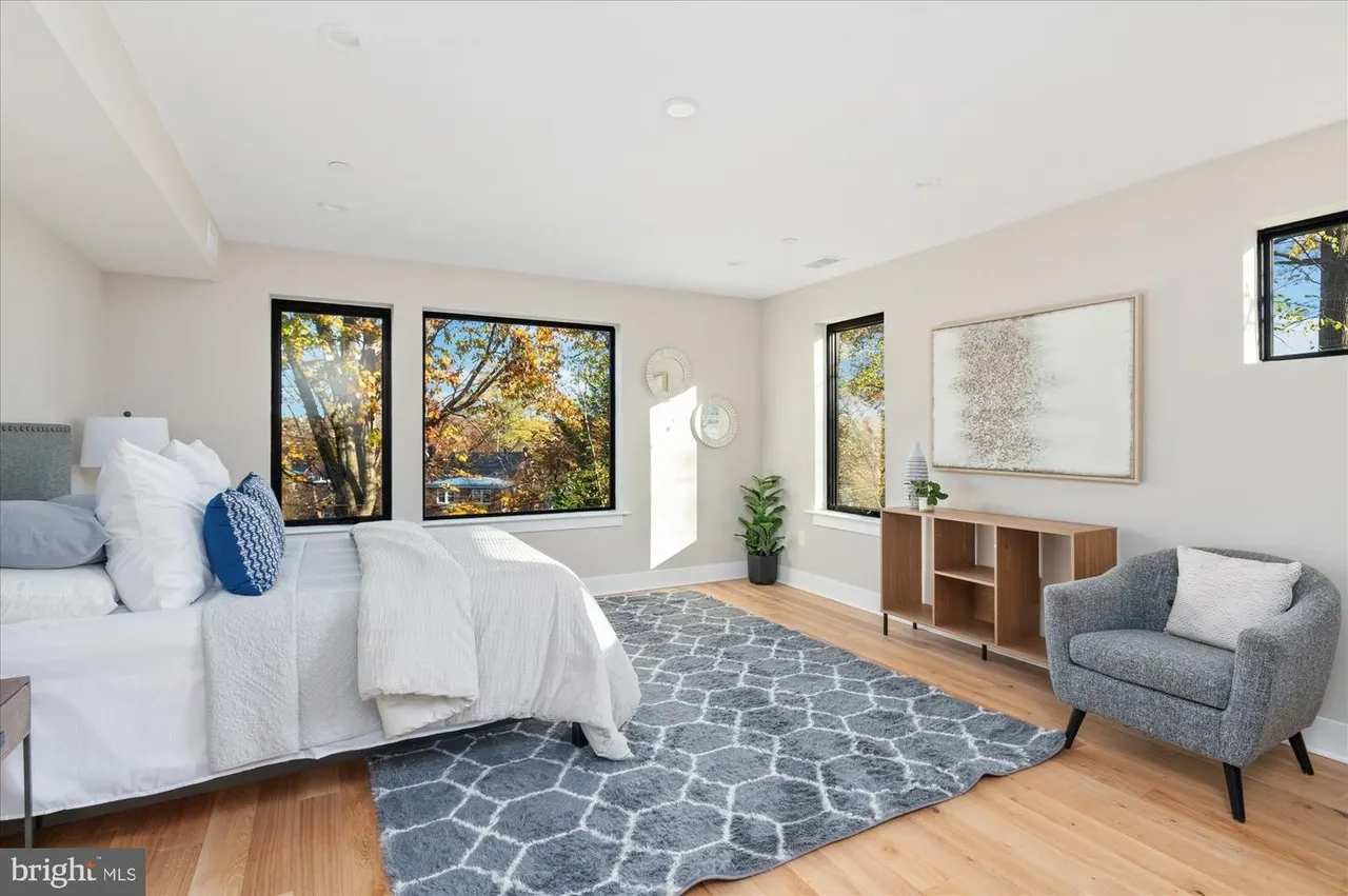 Primary bedroom with white bedding and multiple windows overlooking trees
