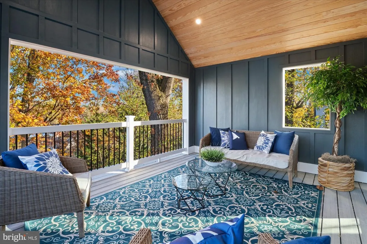 Covered deck with wicker seating, blue patterned rug, and railings
