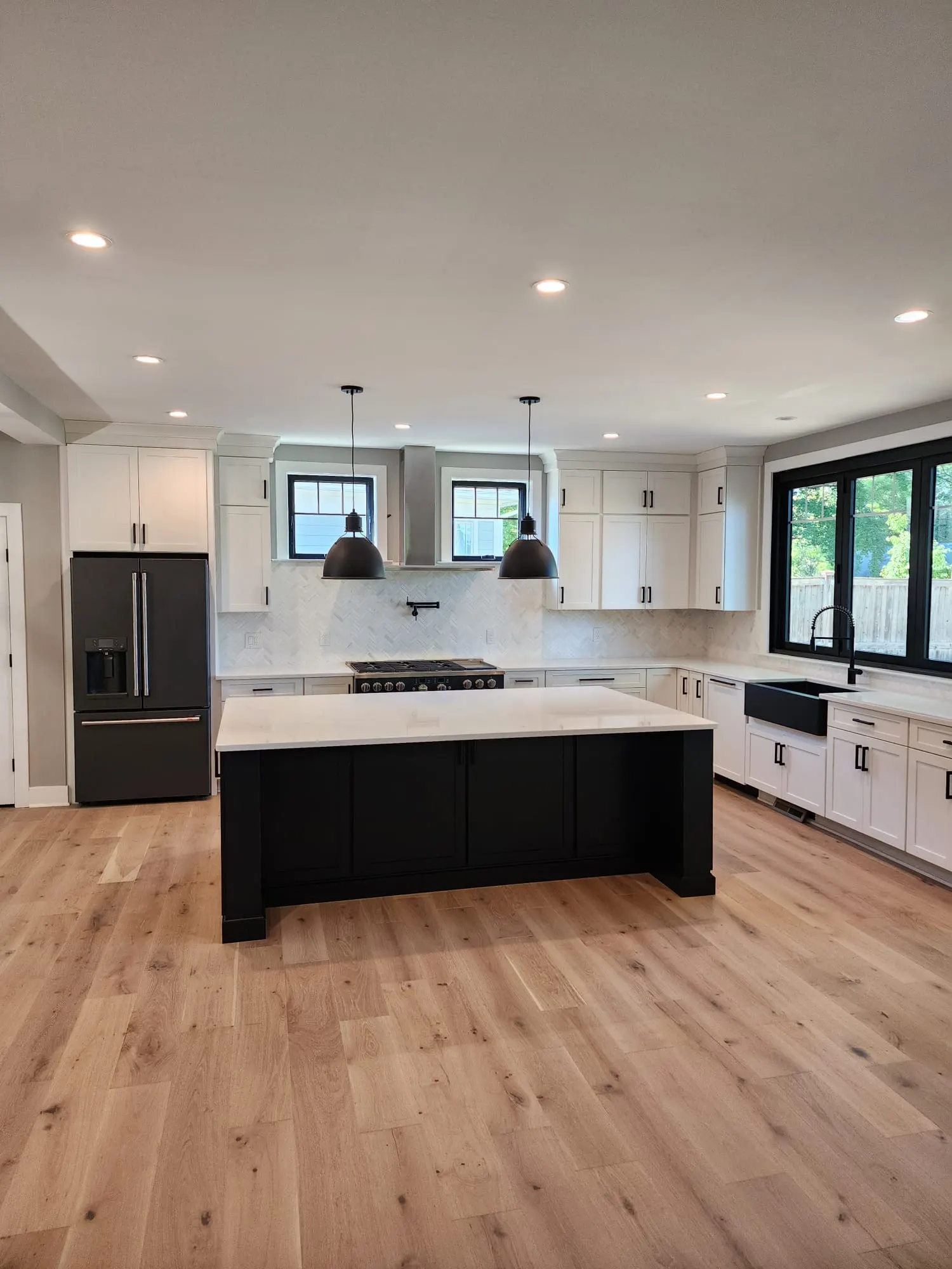 White kitchen with black island, pendant lights, and oak floors