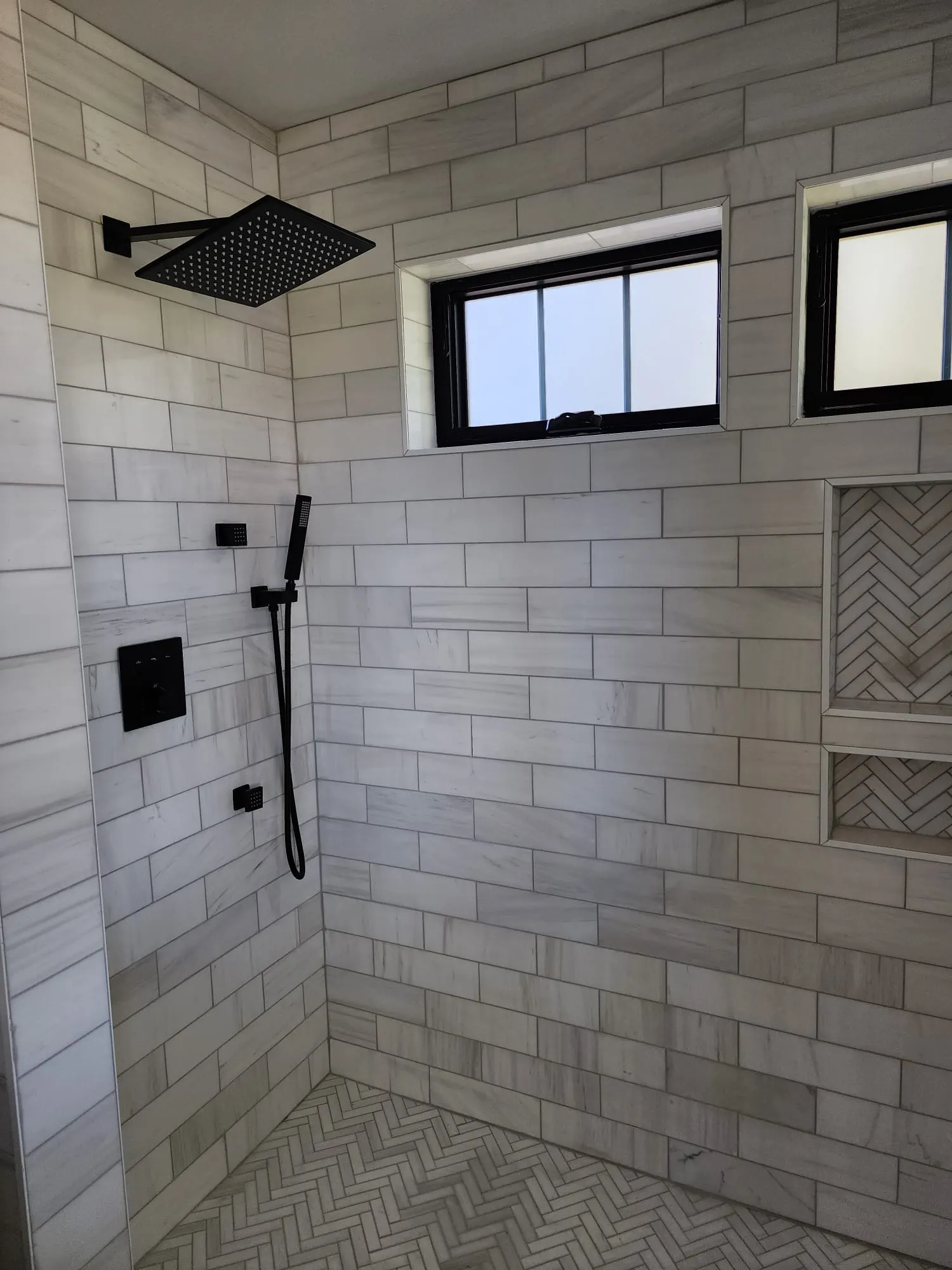 Walk-in shower with marble tile, black fixtures, herringbone niche