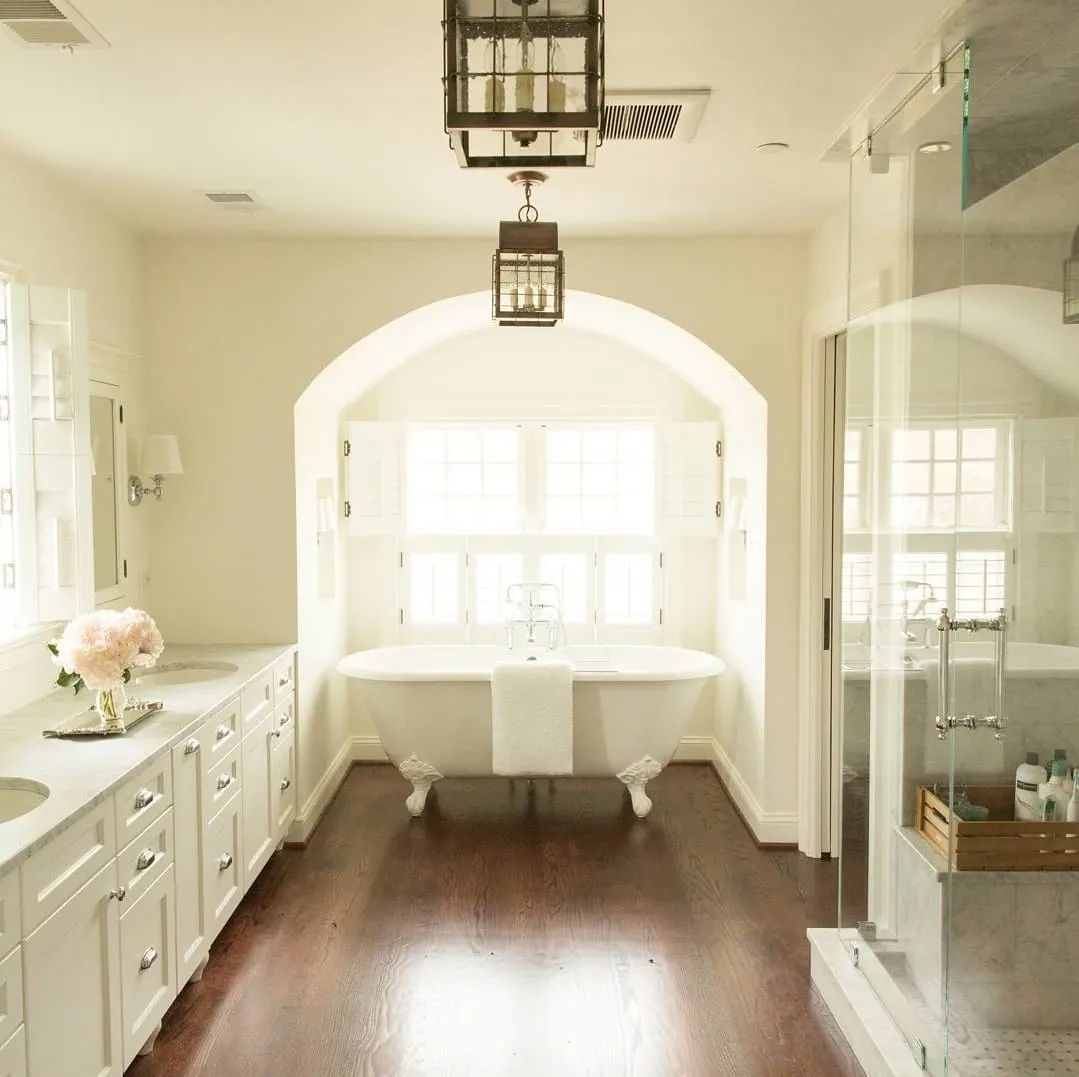 Clawfoot tub in arched alcove with double vanity and glass shower