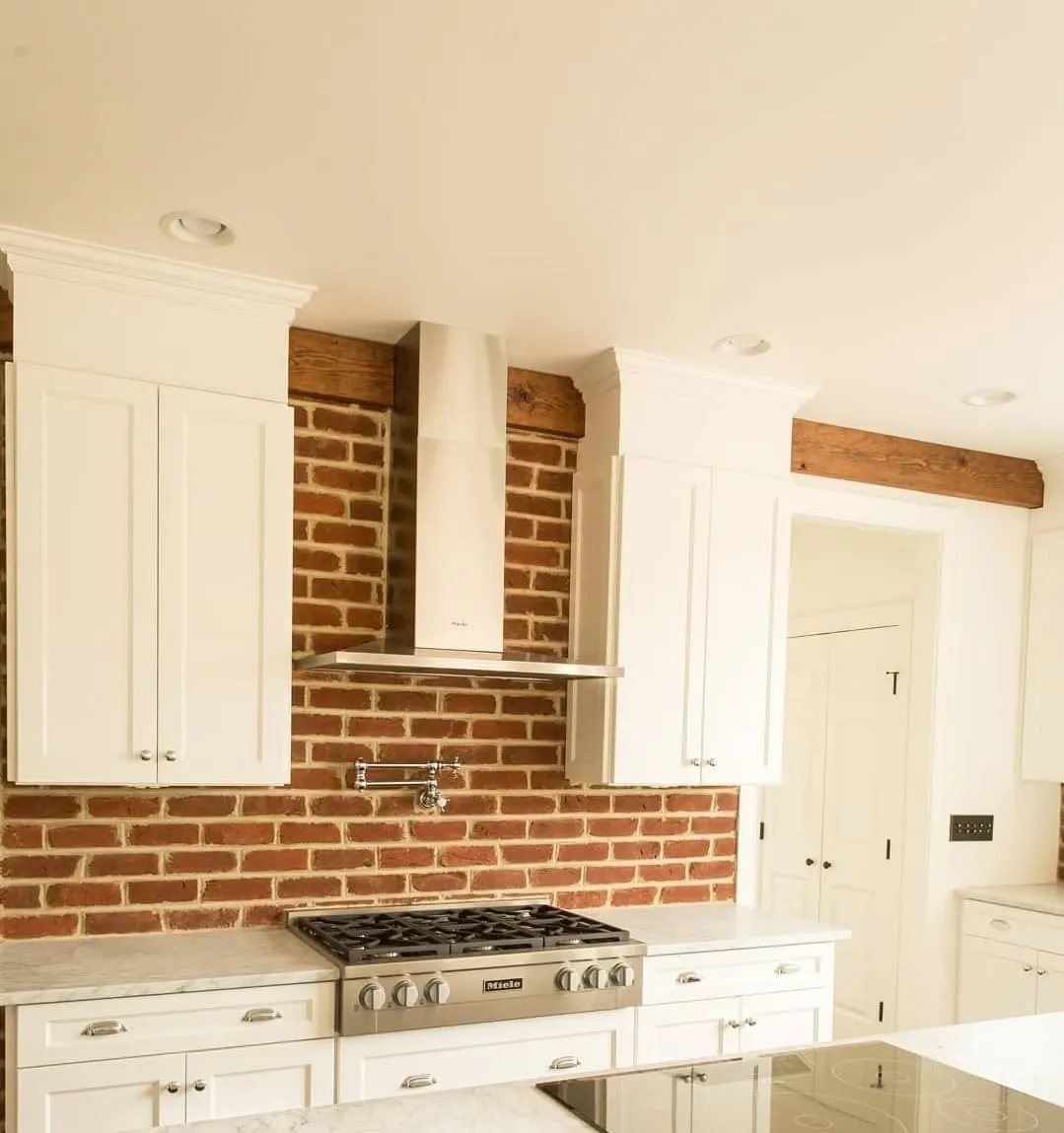 White kitchen with exposed brick backsplash, gas rangetop, and wood beams