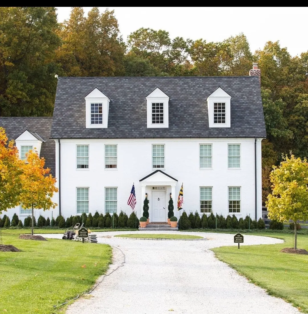 White brick colonial with dormers and gravel circular driveway