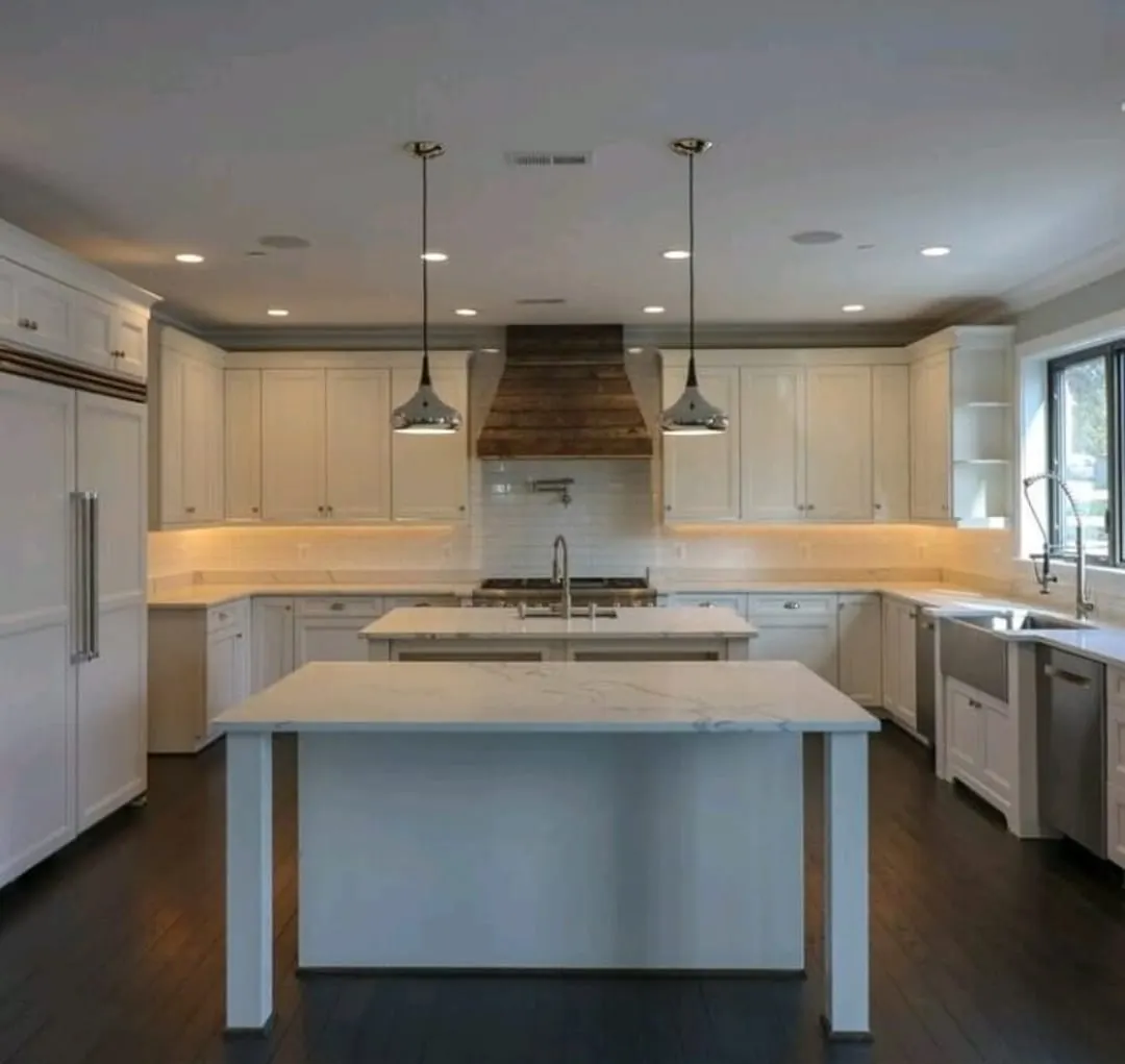 White kitchen with two islands, wood range hood, pendant lights