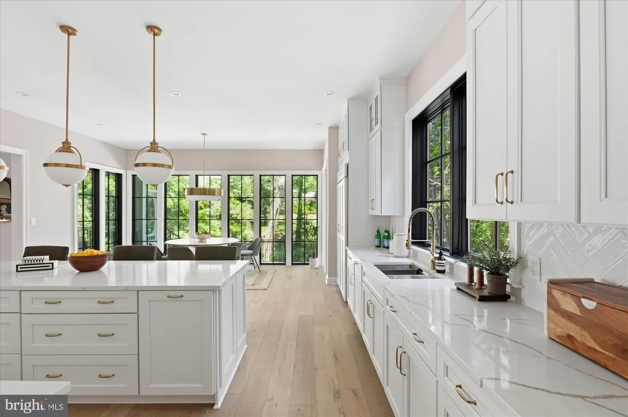 White kitchen with island, brass pendants, and black-frame windows