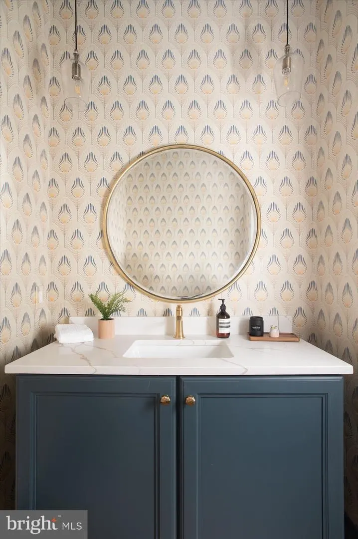 Bathroom vanity with patterned wallpaper, round mirror, brass fixtures