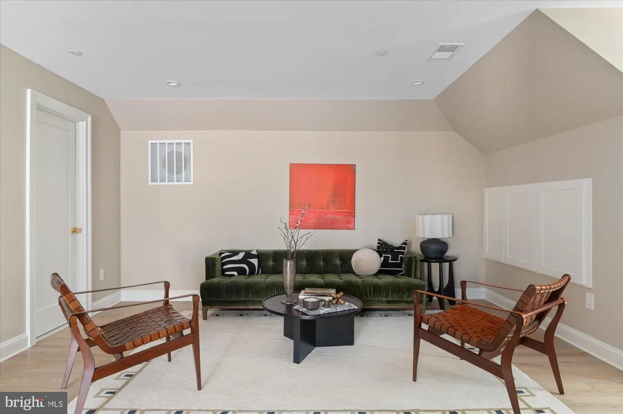 Living room with green sectional sofa, wood chairs, and red artwork