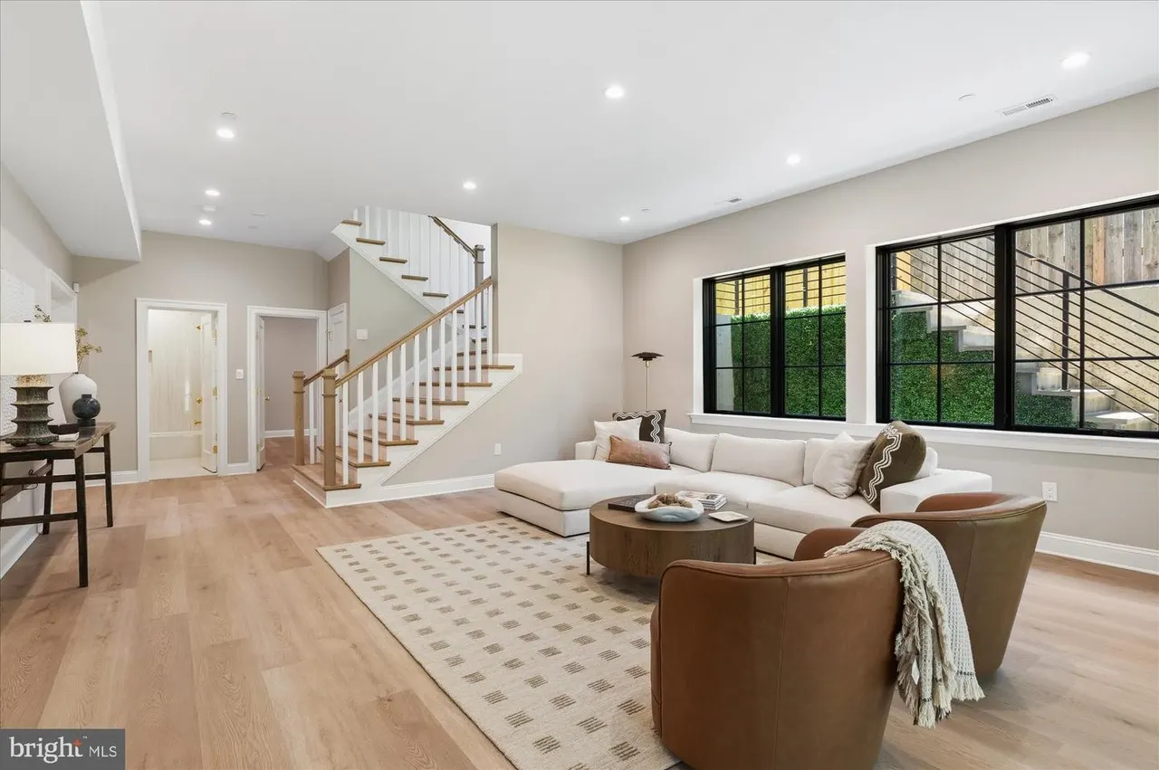 Open-concept living room with cream sofa, staircase, and black-framed windows