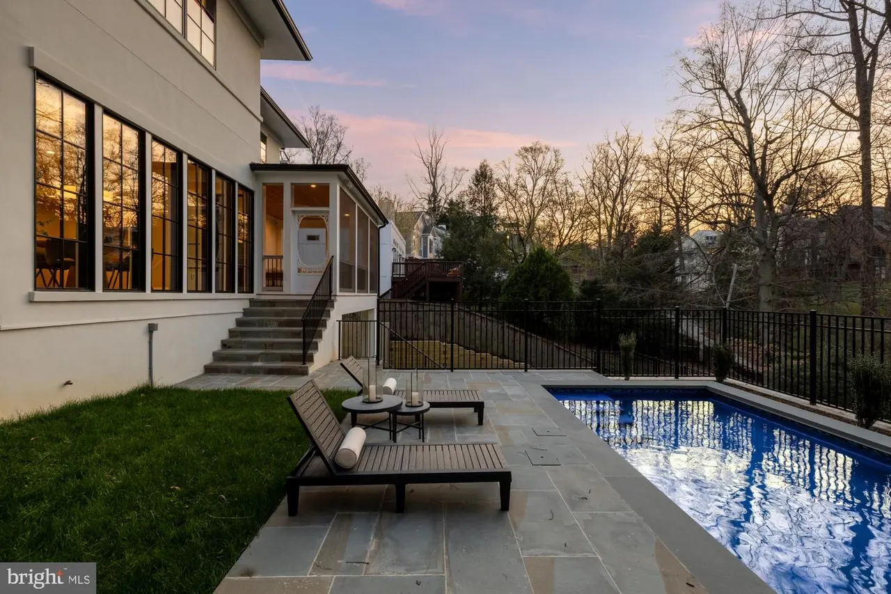 Pool deck with lounge chairs, lawn, and house exterior at dusk