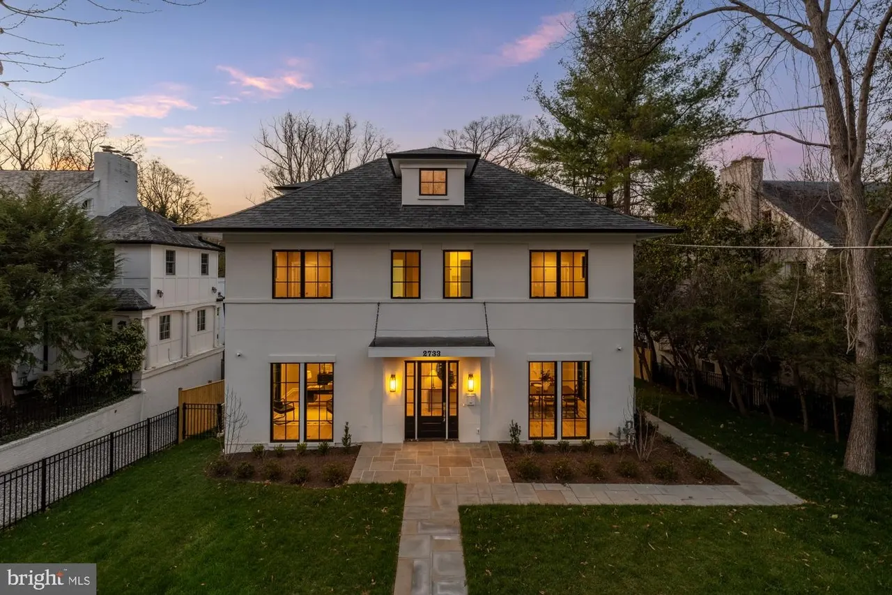 White modern house facade with black roof and lit windows at dusk