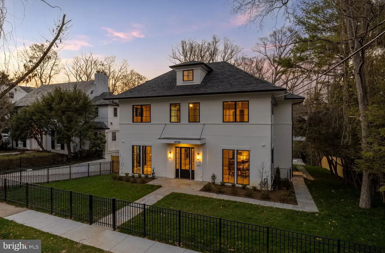 Two-story white house with black trim and metal fence at dusk
