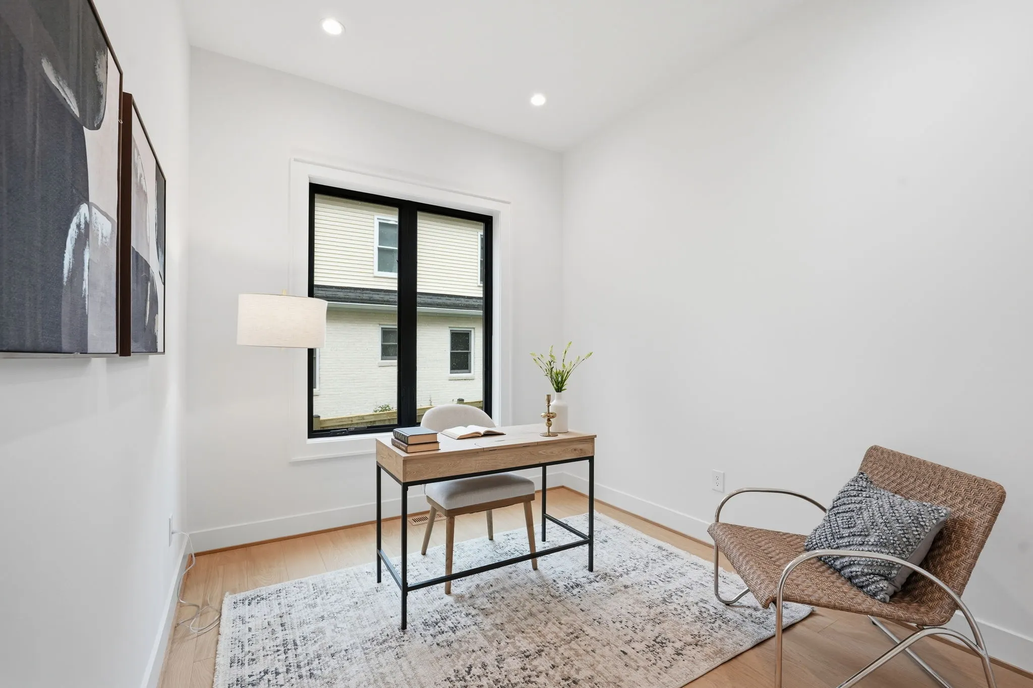 Home office with wooden desk, woven chair, and black-framed window