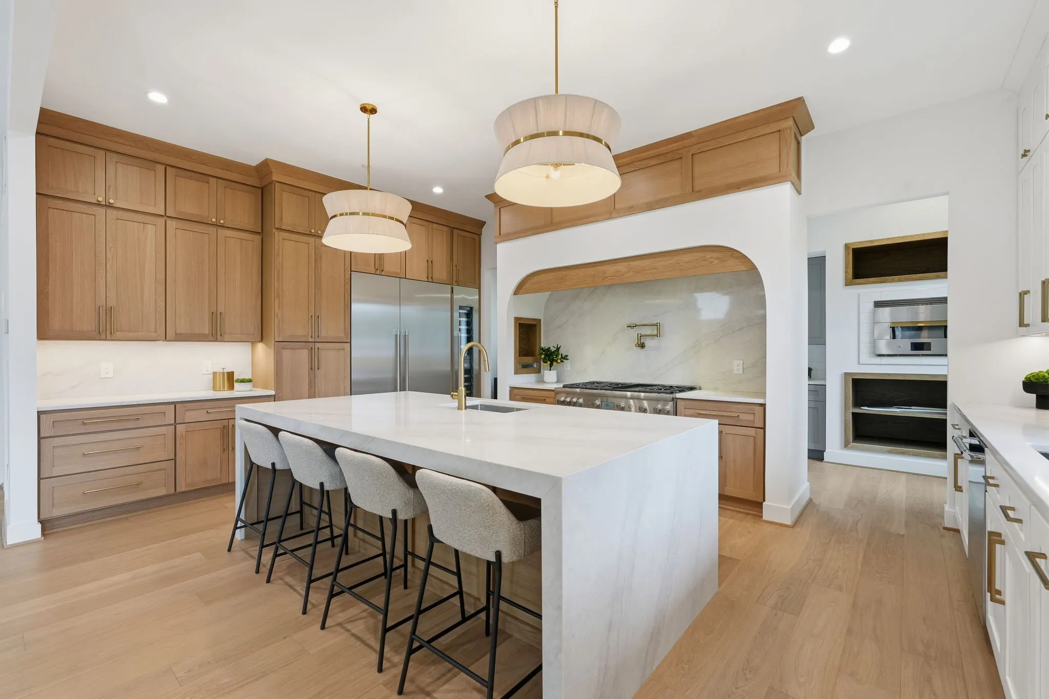 Kitchen with white island, wood cabinetry, pendant lights, bar seating