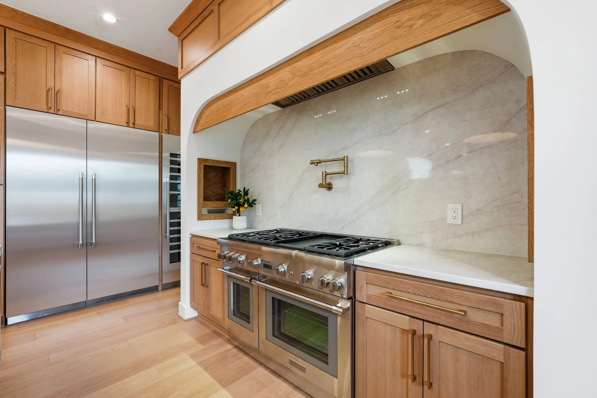 Kitchen detail with wood cabinetry, range hood, marble backsplash, built-in appliances