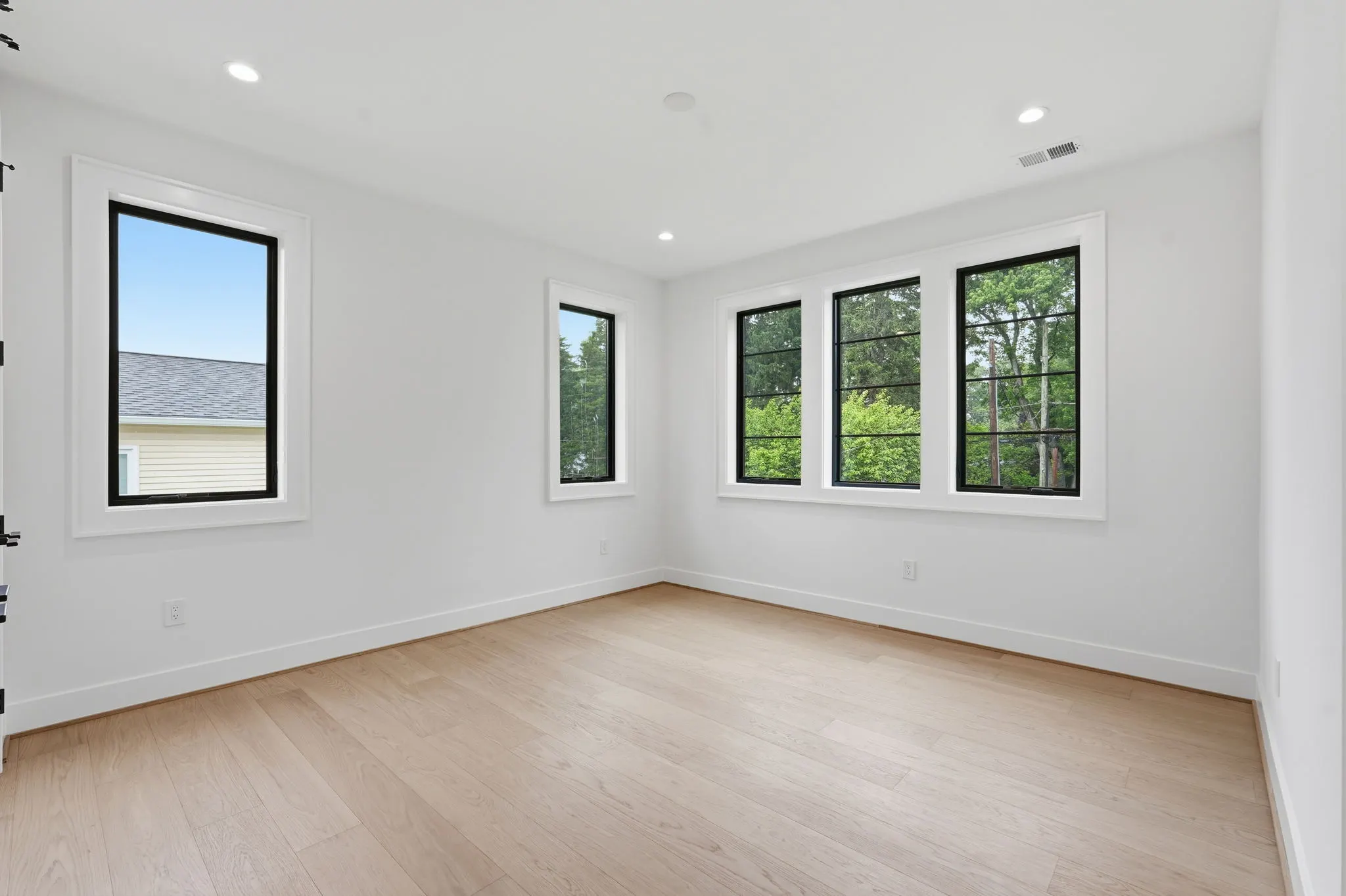 Empty bedroom with wood flooring and multiple black-framed windows