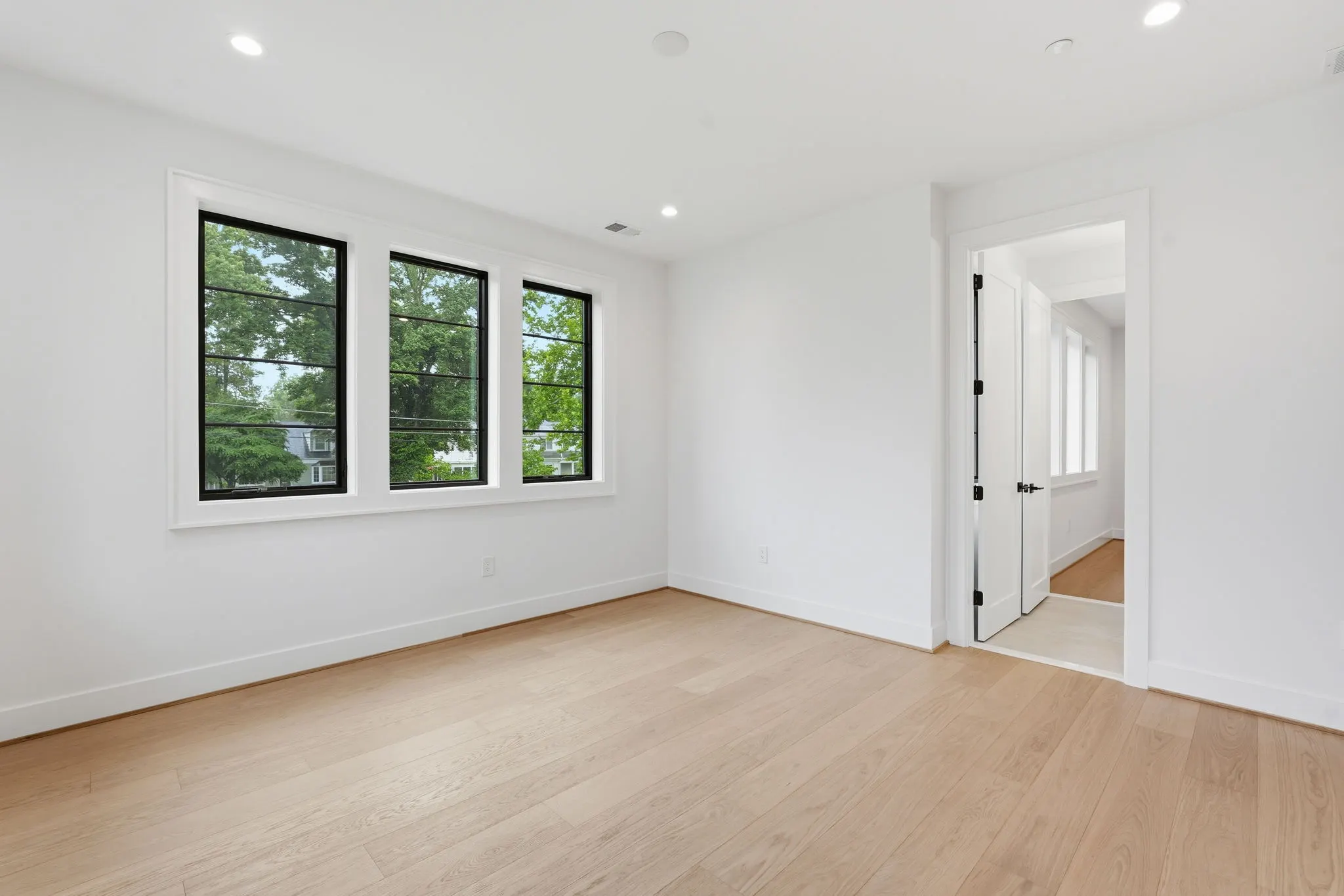Bedroom with wood flooring, triple windows, and white door to hallway