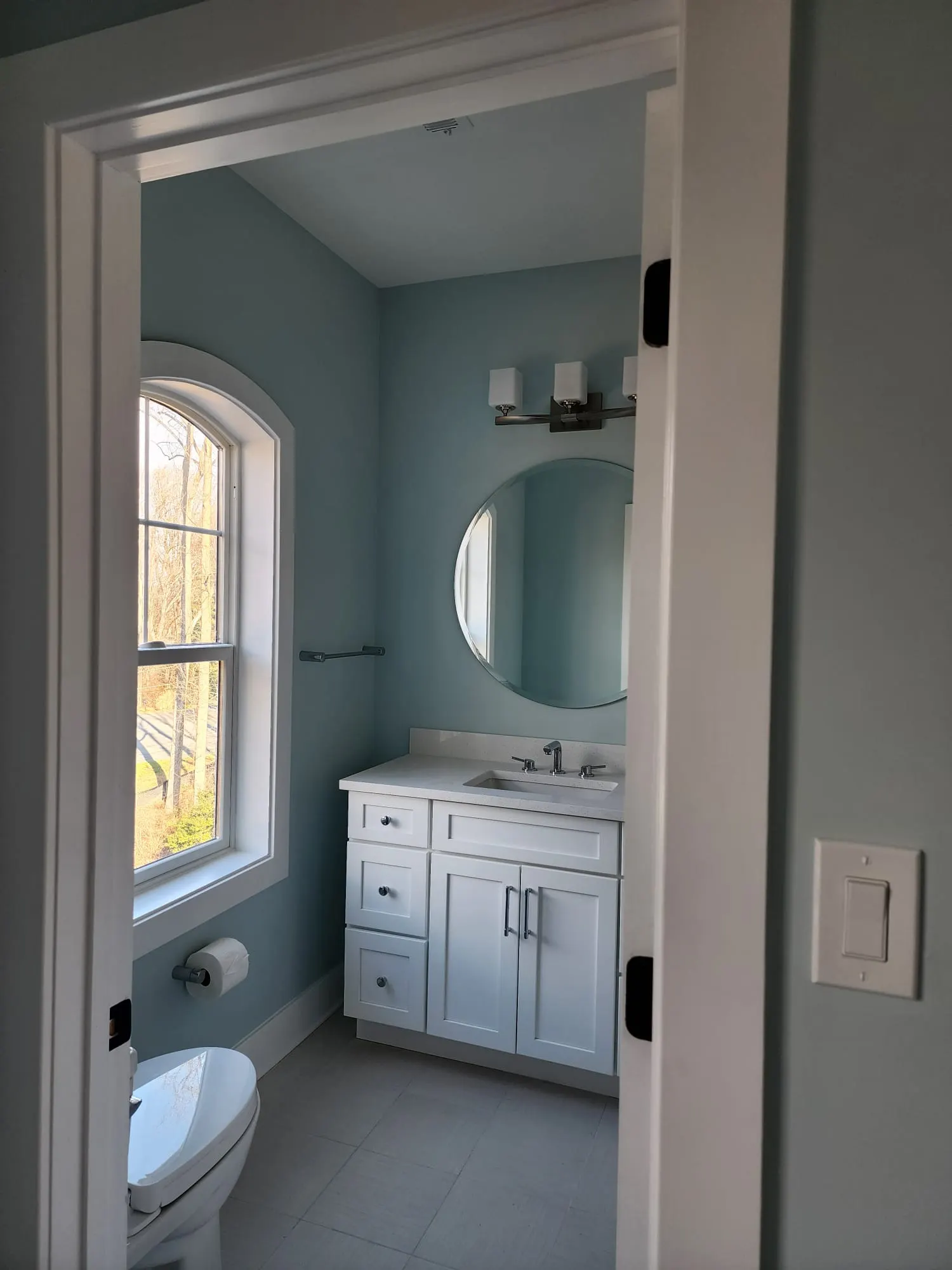 Bathroom with arched window, round mirror, white vanity