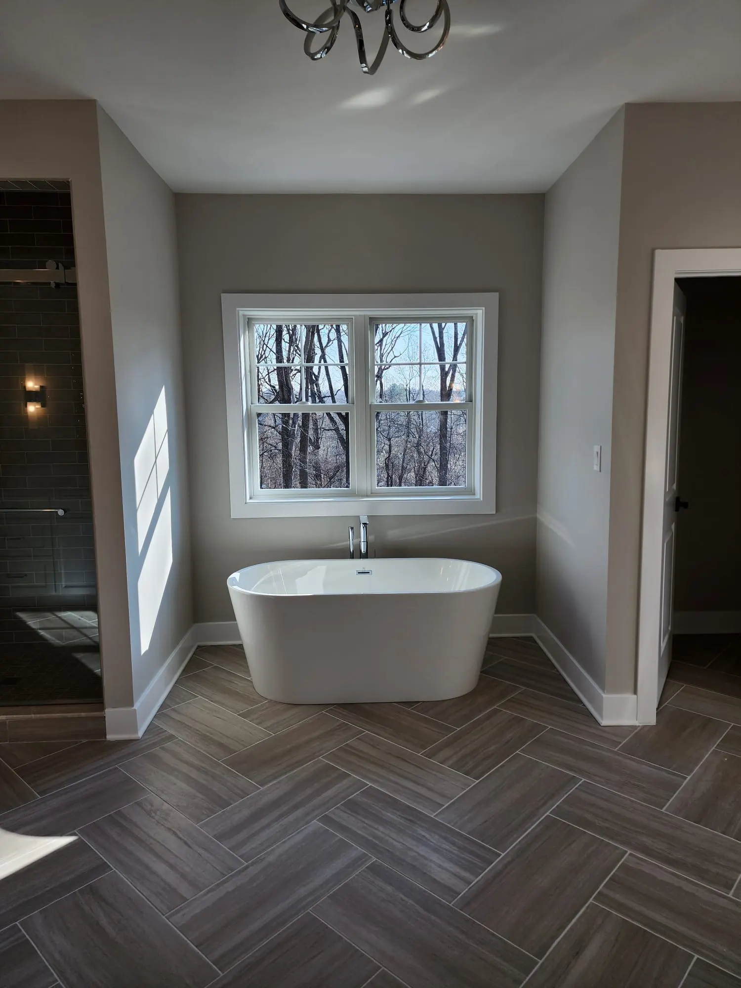 Freestanding tub under window with herringbone tile floor