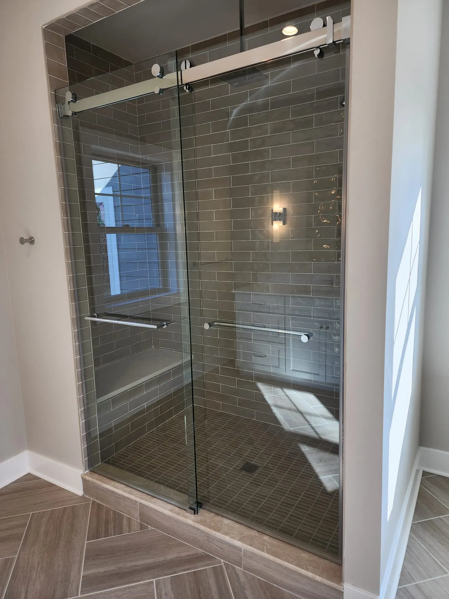 Glass shower with gray subway tile and bench