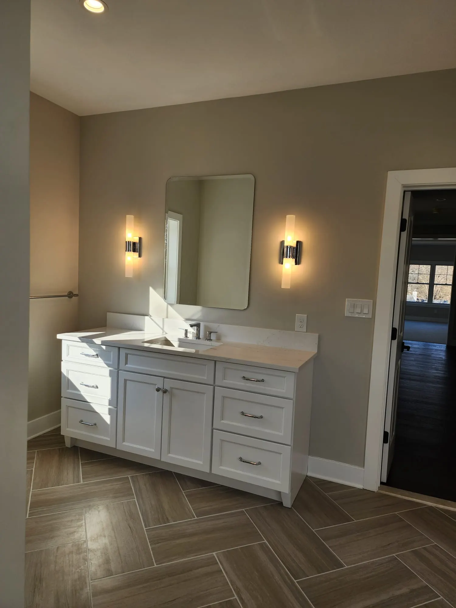 White vanity with tube sconces and herringbone tile floor