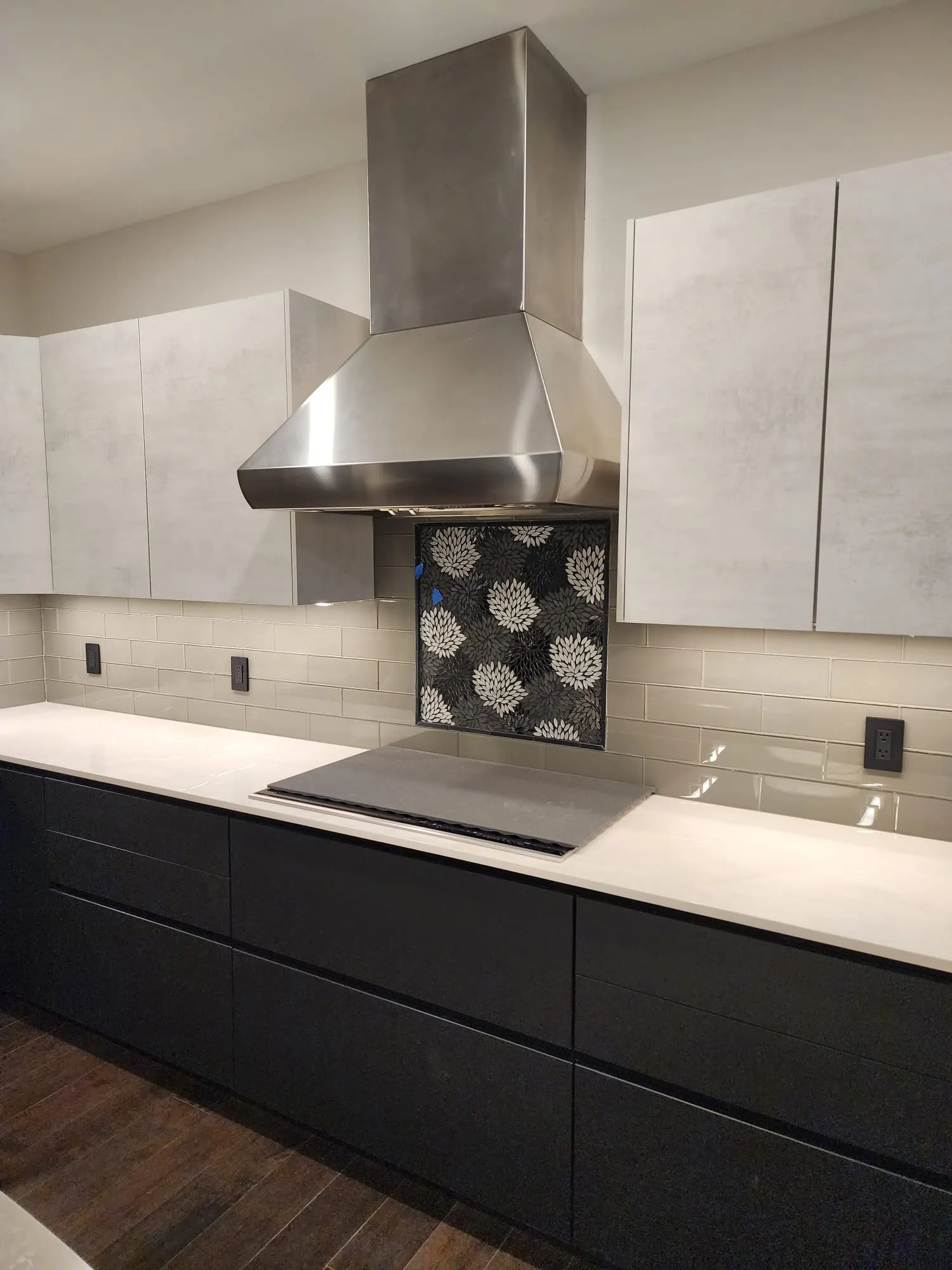 Stainless range hood over floral mosaic tile backsplash