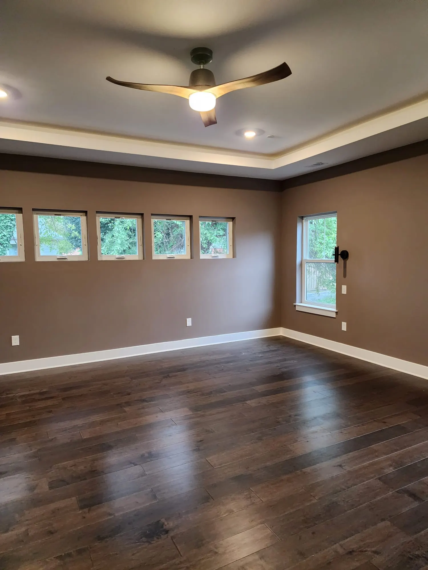Empty bedroom with tray ceiling, ceiling fan, dark wood floors