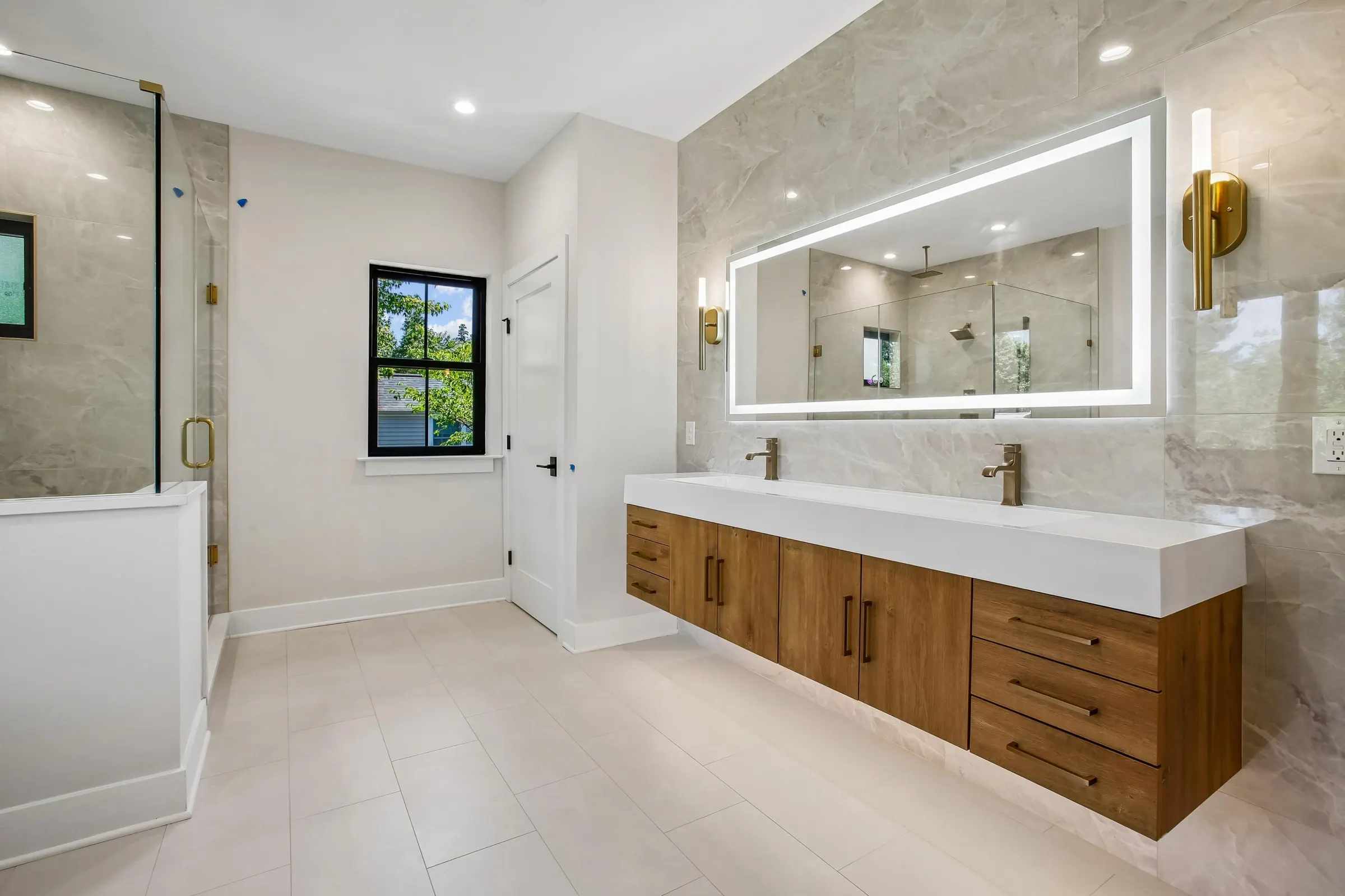 Primary bathroom with floating oak double vanity, backlit mirror, and glass shower