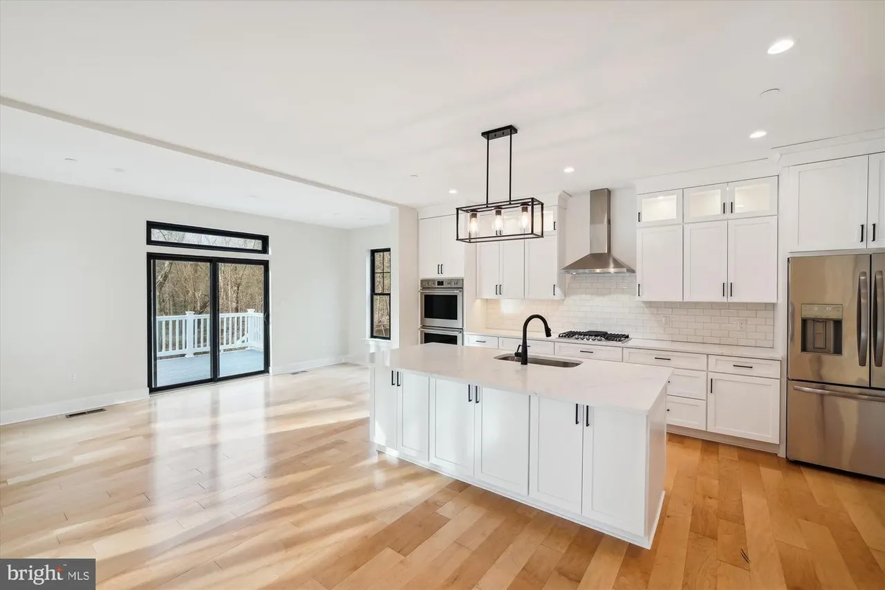 White kitchen with island, range hood, and glass doors to deck