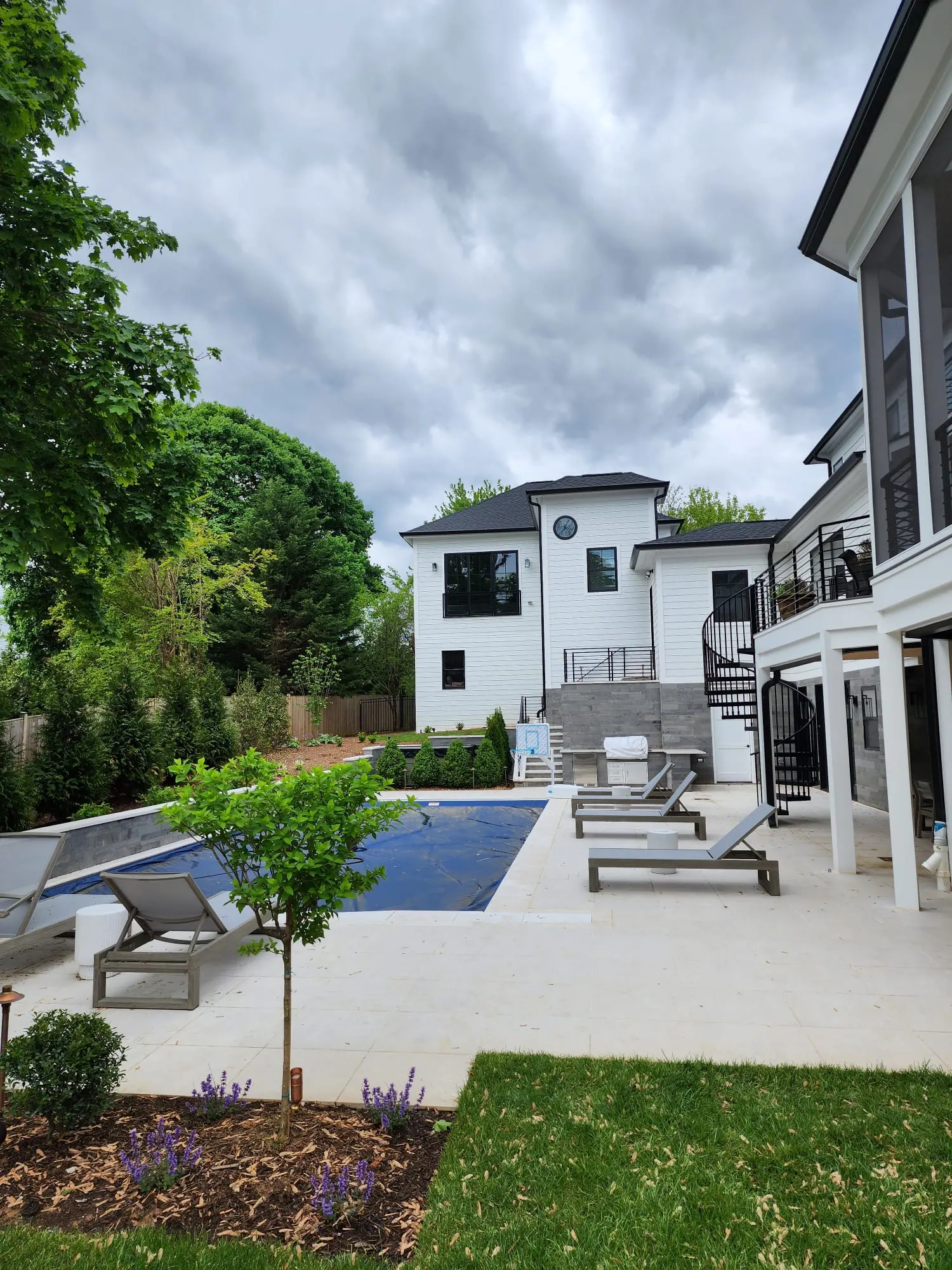Backyard pool with cover, stone patio, and fenced landscaped yard