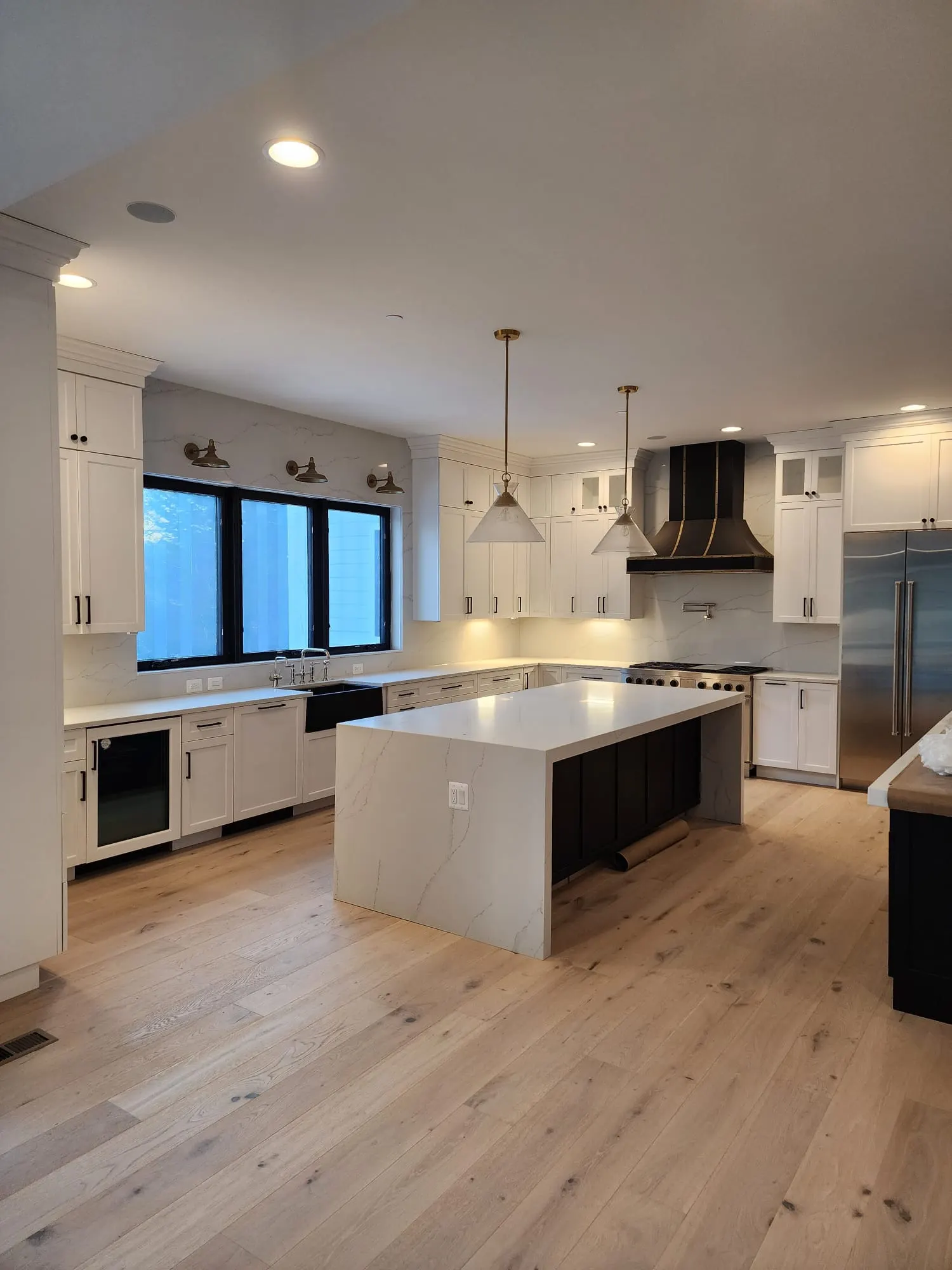 Kitchen with white cabinets, quartz waterfall island, and black range hood