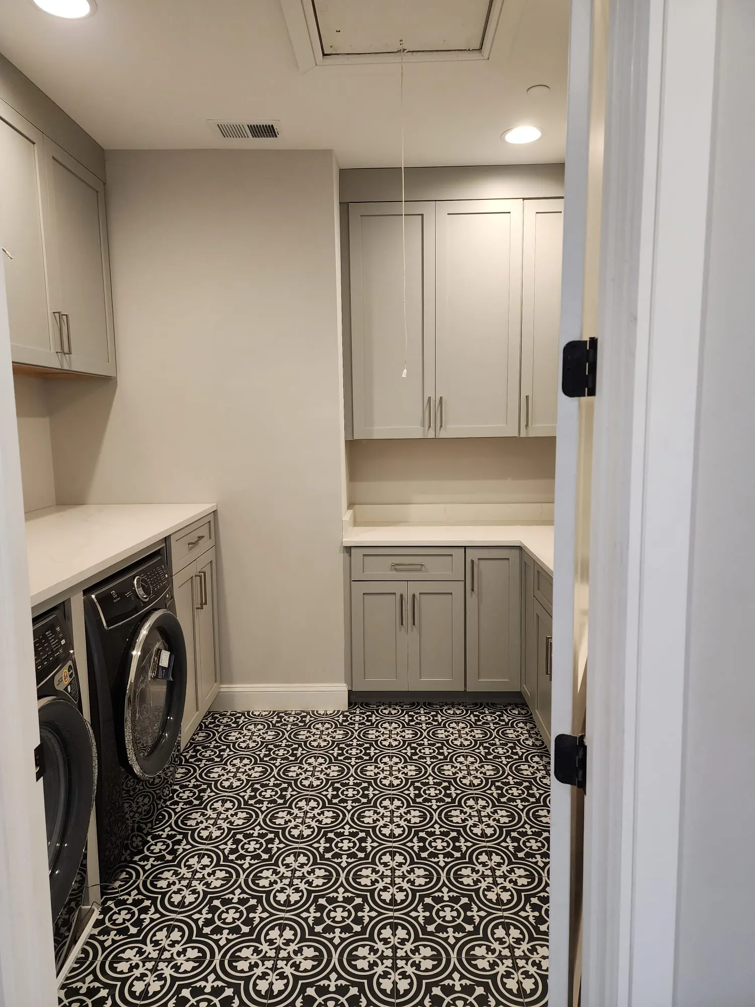 Laundry room with gray cabinets and patterned black-and-white tile floor