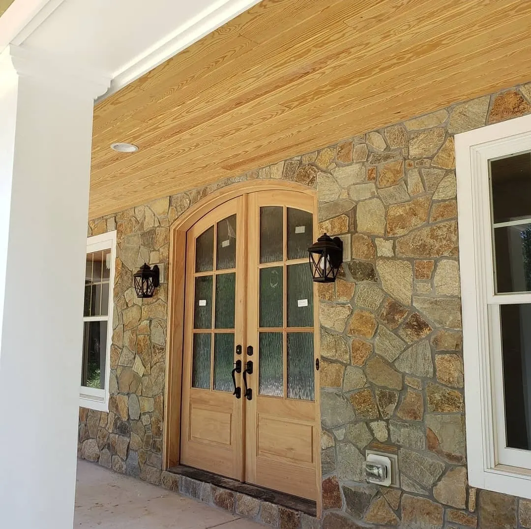 Arched wood double front doors framed by stone and wood ceiling
